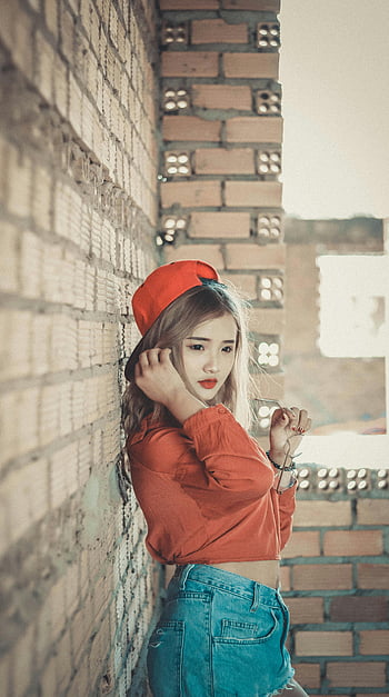 오렌지 탑의 소녀, 갈색 콘크리트 벽돌, 세련되게 옷을 입었습니다, 젊은 여성, 캐주얼 복장, 벽돌 벽, 포즈를 취하는, 오렌지 모자, 데님 반바지, 도시 스타일, 거리 패션