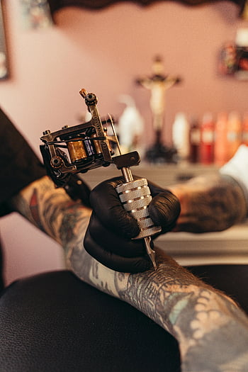 tattoo artist, arm tattoo, tattoo studio, close-up, tattoo machine, black gloves, client arm, tattoo process, studio setting, artistic work, body art