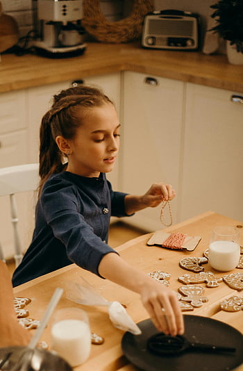 Dívka zdobení perníku, Útulná kuchyně, prázdninová sezóna, pečení dítěte, perník cookies, Slavnostní atmosféra, kuchyňský stůl, dovolená pečení, mladá dívka, útulný domov, mléko a sušenky