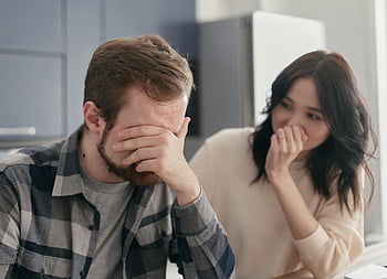 Homme en chemise à carreaux, visage couvrant, couple désemparé, stress intérieur, préoccupation, empathie, moment émotionnel, couple en détresse, scène intérieure, Expression émotionnelle, chemise à carreaux