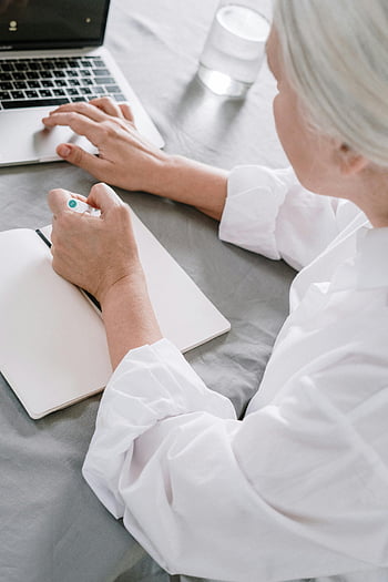 oudere vrouw, Notities nemen, laptop gebruiken, thuis, werkend, senior, technologie, notitieboekje, glas water, gefocust, produktief