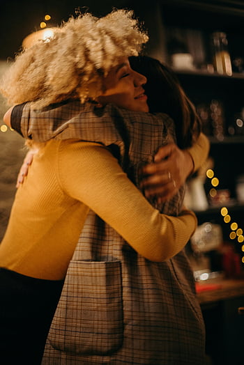 ženy objímání, Slavnostní světla, teplé objetí, Vnitřní nastavení, dvě ženy, emoční okamžik, Atmosféra prázdnin, Útulná scéna, přátelství, jednotnost, oslava