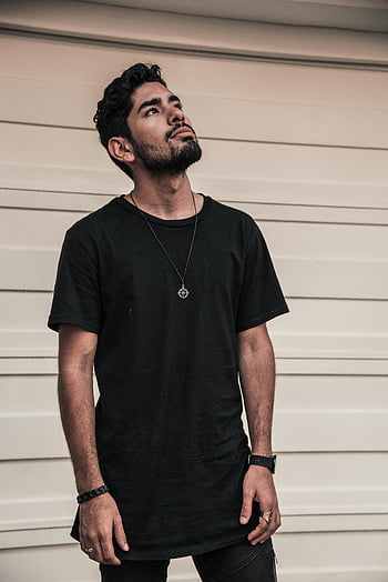 Mand i sort t-shirt, hvid væg, kigger op, afslappet tøj, moderigtig mand, sort besætning hals, stående, udendørs, stilfuld, moderne mode, tilbehør