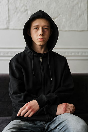 Teenager, schwarzer Kapuzenpullover, Sitzung, Schwarze Couch, drinnen, Ernsthafter Ausdruck, nachdenklich, Legere Kleidung, Jugendmode, Innenumgebung, Entspannte Pose