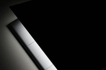 black background, modern laptop, sleek design, shadow, close-up view, partial view, laptop closed, minimalist design, dark aesthetic, technology, modern device