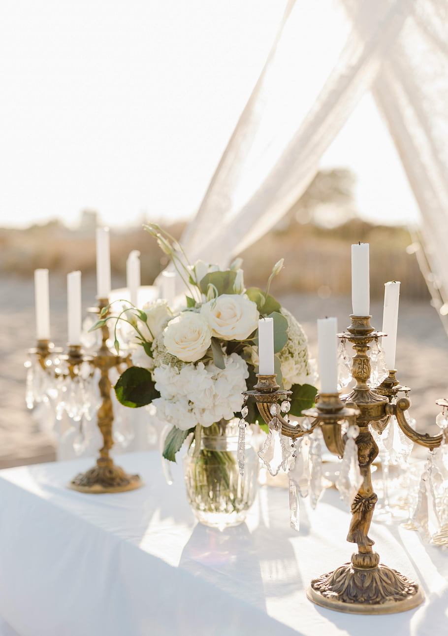 elegant candle holders, white bouquet, floral centerpiece, vintage candlesticks, outdoor wedding table, luxurious table setting, white flowers, crystal accents, wedding decor, romantic setting, outdoor wedding