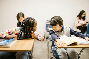 elementary students, classroom setting, chatting, communication skills, two students, gossiping, desks, books, learning environment, interaction, education