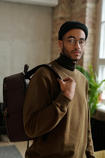 Hombre con abrigo marrón, gorra negra, lentes, mochila, retrato de interior, estilo urbano, hombre joven, retrato contemporáneo, entorno interior, Atuendo casual, aspecto moderno