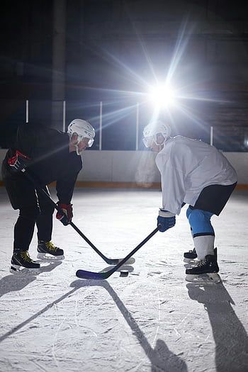 men playing hockey, indoor ice hockey, dramatic lighting, two players, facing off, ice rink, hockey sticks, helmets, sports action, ice skating, competition