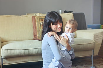 Žena v šedém svetru, přenášení batole, Bílá knoflíková košile, Matka objala dítě, vnitřní pohodlí, gauč, teplo, jednotnost, Rodinný okamžik, Domácí nastavení, milovat