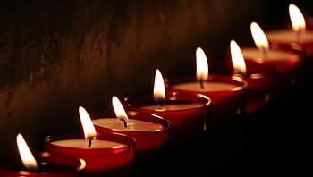 white votive candles, lit candles, warm glow, dark setting, serene atmosphere, candlelight, close-up view, red candle holders, soft lighting, peaceful ambiance, candle arrangement