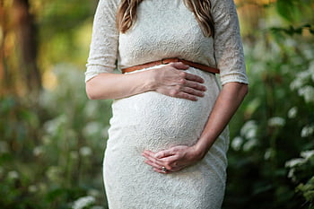 pregnant woman, lace dress, cradling belly, outdoor setting, maternity photoshoot, pregnancy, nature background, gentle touch, belly bump, motherhood, lace fabric