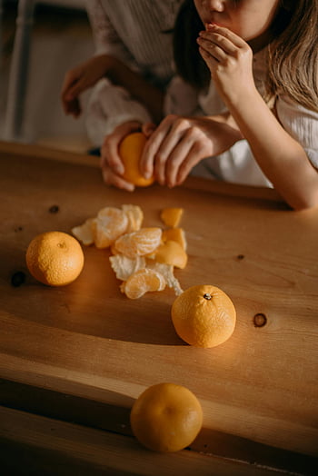 pige spiser orange frugter, Hyggelig scene, mennesker, der interagerer, Friske mandariner, træbord, Varm atmosfære, hjemlig atmosfære, appelsinfrugter, mandariner, træoverflade, hyggelig interaktion