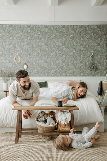 family bonding, cozy bedroom, parents playing, child on floor, family time, playful moment, parents and child, bedroom scene, family interaction, happy family, cozy home