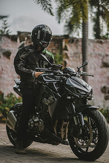 man in black leather jacket, riding motorcycle, Kawasaki bike, stone pavement, motorcyclist, black leather gear, helmet, outdoor setting, motorcycle rider, black motorcycle, street scene