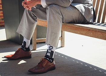man sitting on bench, businessman, grey suit, unique socks, personality, bench, outdoor, formal wear, stylish socks, brown shoes, casual setting