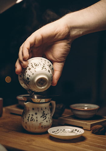 tea ceremony, traditional Chinese teacup, pouring tea, white ceramic saucer, brown wooden table, indoor tea ceremony, hand pouring tea, cozy setting, Chinese tea culture, tea preparation, teapot