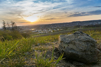 gray stone, grassy field, cloudy sky, sunset, close-up rock, scenic background, natural landscape, outdoor scene, evening light, rural view, horizon line