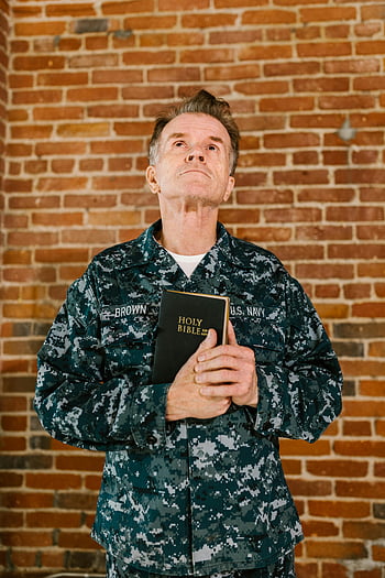 soldato della Marina degli Stati Uniti, alzando lo sguardo, Tenendo la Bibbia, veterano anziano, muro di mattoni, Sacra Bibbia, uniforme militare, momento spirituale, fede, religioso, contemplazione