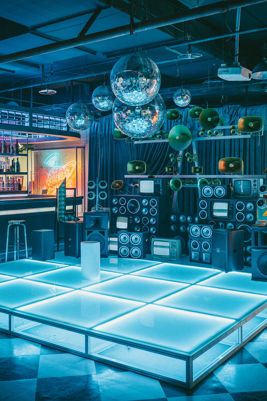 disco koule, noční klub, retro interiér, neonová světla, vinobraní výzdoba, živá atmosféra, taneční parket, reproduktory, televizní přijímače, modré osvětlení, retro výzdoba