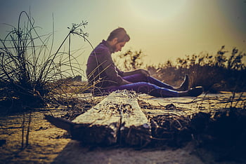 man sitting, brown wood plank, sandy terrain, sunset, solitude, nature's calm, outdoor scene, peaceful moment, natural setting, serene environment, lone figure