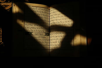 Corano aperto, testo santo, luce calda, impostazione intima, ombre, libro religioso, Scritture islamiche, lettura spirituale, pagine sacre, Versi coranici, luce spirituale