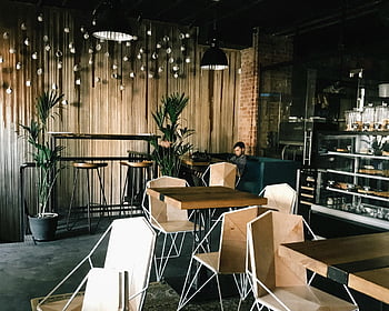 Mann sitzt, Cafe, Modernes Café, Geometrische Stühle, Pflanzen, warmes Licht, Entspannte Atmosphäre, Stylish Cafe, Holztische, Innencafé, gemütliches Café