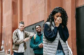 multiethnic male students, gossiping, sad crying woman, teenager upset, peers mocking, urban setting, bullying issues, emotional distress, social issues, peer interaction, outdoor scene
