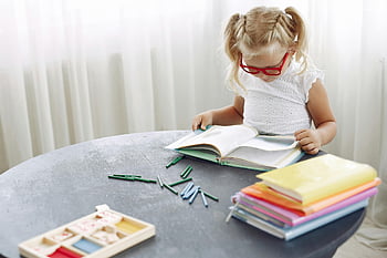 focused girl, reading book, home table, young girl, glasses, concentrated reading, books, crayons, home study, child education, indoor activity