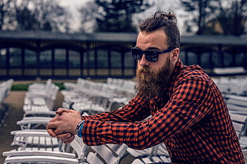 vousatý muž, kostkovanou košili, černé wayfarer sluneční brýle, bílá dřevěná židle, venku, Hipster Vibe, černá a červená kostkovaná, tričko s dlouhým rukávem, sedící, sluneční brýle, dřevěná židle