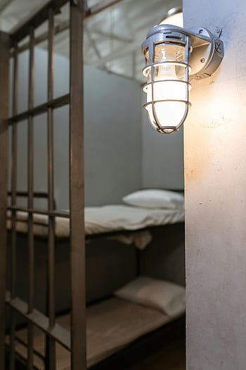 jail cell, illuminated wall lamp, concrete wall, steel bars, steel bunk bed, industrial wall lamp, interior, prison, cell, lighting, bars