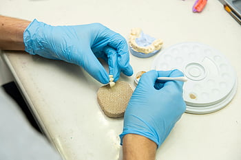 zubní technik, Implantát keramického zubu, Laboratorní nastavení, detail, řemeslné práce, zubní implantáty, Aless Mistr, modré rukavice, Dentální protetika, obnovení zubů, Dental Lab