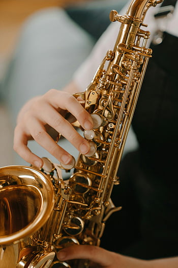 gold saxophone, black background, close-up, child playing, musical details, saxophone keys, brass instrument, musical instrument, young musician, saxophone player, music performance