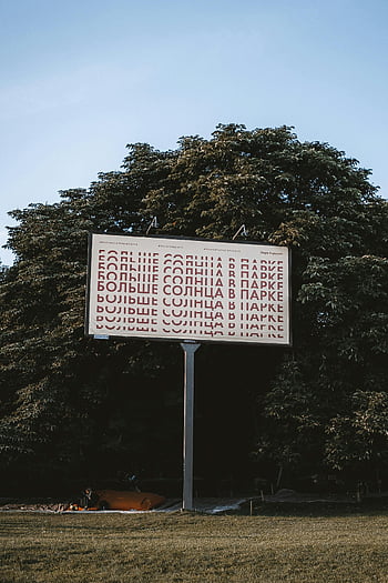 Plakatwand, Schriften, draussen, üppiges Grün, sonniger Tag, Große Werbetafel, Prominente Anzeige, natürliche Umgebung, Parkszene, Textdesign, Landschafts Hintergrund