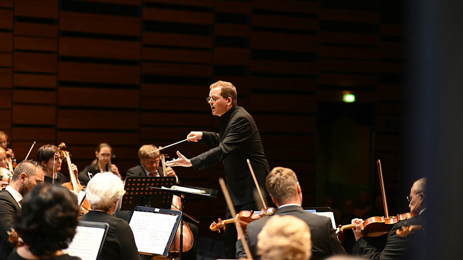 orchestra, conductor, classical music, live performance, indoor concert, musicians, symphony, music conductor, stage performance, musical instruments, audience