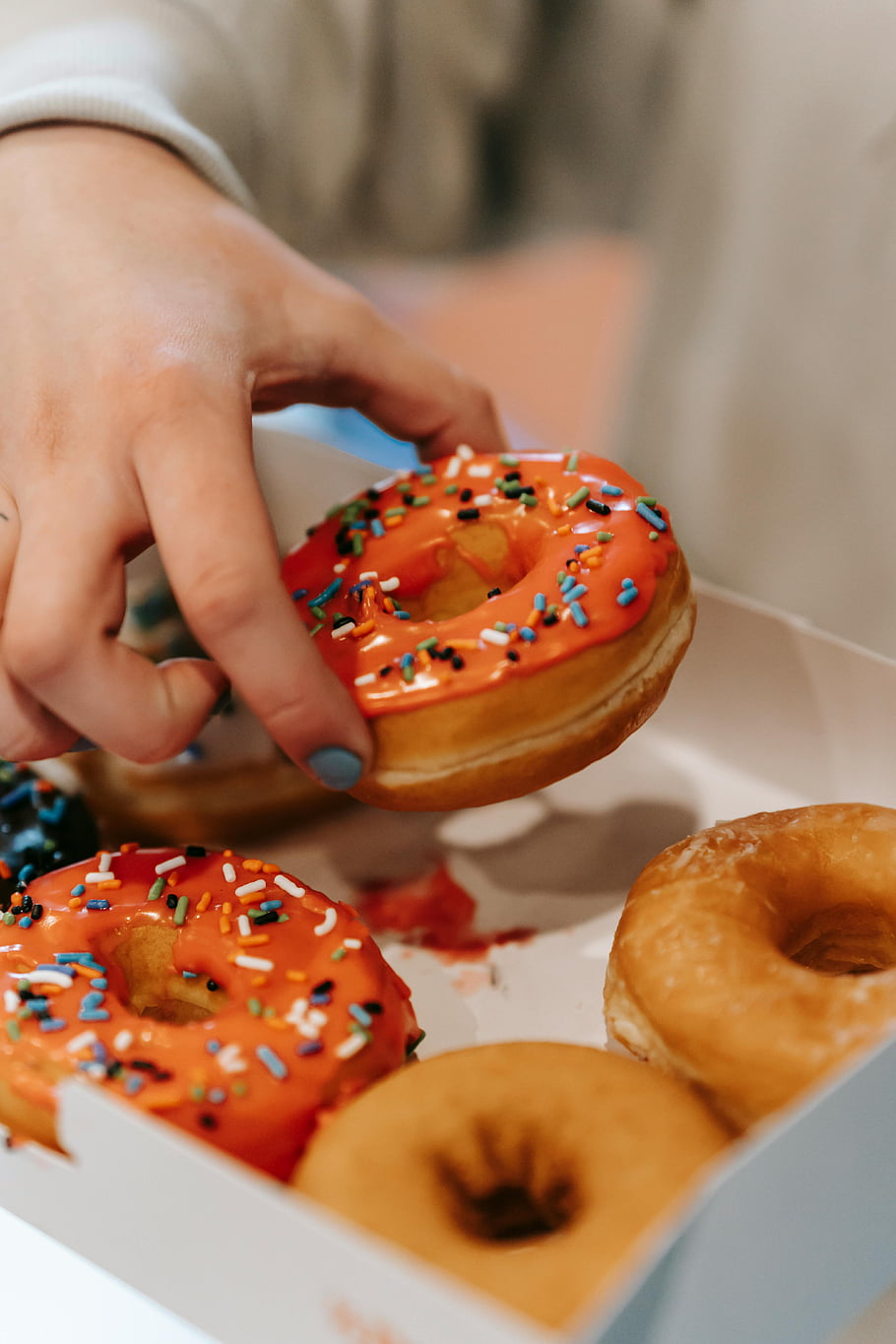 donuts, colorful sprinkles, picking donut, box of donuts, vibrant donuts, close-up donuts, yummy donut, unrecognizable woman, donut box, donut selection, donut variety