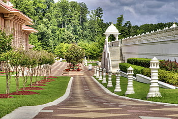 peaceful garden, ornate architecture, lush greenery, sunny day, white pillars, concrete hallway, building view, outdoor scene, landscaped garden, cultural architecture, serene environment