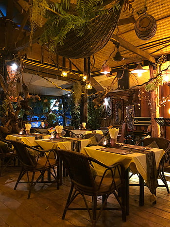 restaurace stůl, židle, rustikální prostředí, teplé osvětlení, dekorativní rostliny, Útulné stolování, Okouzlující atmosféra, Vnitřní restaurace, dřevěný nábytek, Tropická dekorace, Večerní stolování
