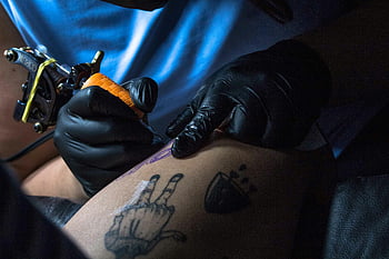 tattoo artist, close-up view, tattooing, design on skin, studio, black gloves, tattoo machine, body art, skin, studio lighting, tattoo process
