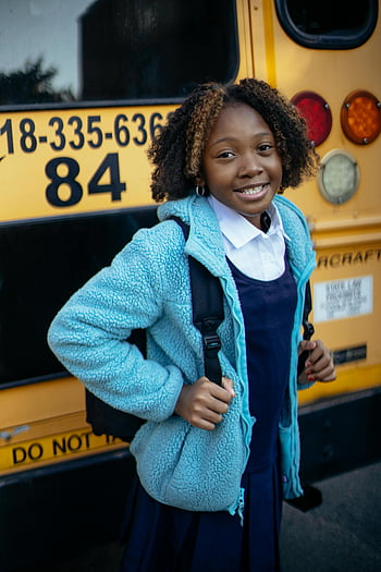 black schoolgirl, smiling schoolgirl, school uniform, yellow school bus, urban setting, street, charming, backpack, blue jacket, curly hair, school day
