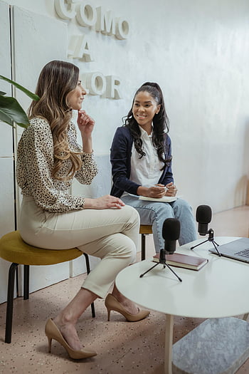 podcast recording, diverse women, modern studio, cheerful conversation, hosting podcast, two women, studio setting, microphones, professional setting, casual attire, engaging discussion