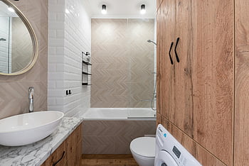 çağdaş banyo, çamaşır makinesi, oval şekilli ayna, ahşap dolap, beyaz armatürler, modern aydınlatma, mermer tezgah, cam duş, şık tasarım, Banyo Tasarımı, Çağdaş tasarım