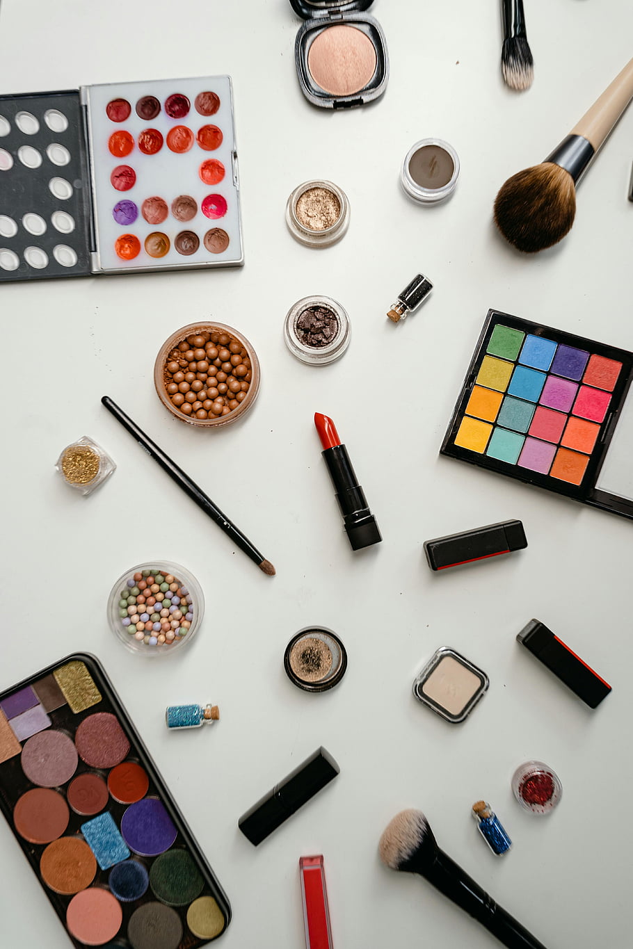 kosmetické výrobky, Sortiment make -upu, palety očních stínů, štětce, rtěnky, bílý povrch, pohled shora, vícebarevný make -up, kosmetika, Nástroje krásy, Sbírka make -upu