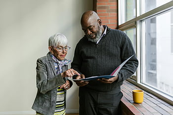elderly man, elderly woman, conversation, folder, business discussion, documents, office setting, review, interaction, professional meeting, indoor setting