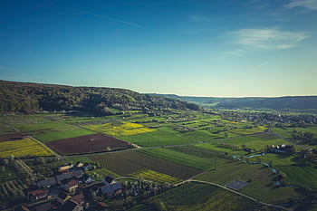 aerial view, green grass field, blue sky, lush green farm fields, distant village, clear blue sky, rural landscape, countryside scenery, farm fields, village view, natural landscape