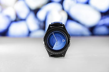 Black Samsung Gear, digital smartwatch, blue interface, abstract blurred background, sleek design, modern watch, white surface, smartwatch display, 05:55 time, stylish watch, digital clock