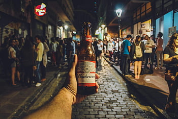 Budweiser bottle, city nightlife, bustling street, crowd, vibrant night, hand holding, beer, urban scene, night scene, street crowd, nightlife atmosphere