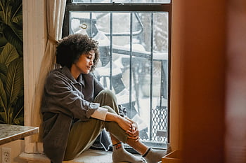 Malinconica femmina nera, Seduto su un davanzale, capelli ricci, Giornata invernale nevosa, riflessione silenziosa, donna per finestra, Scena indoor, umore contemplativo, atmosfera invernale, impostazione accogliente, Vista invernale indoor