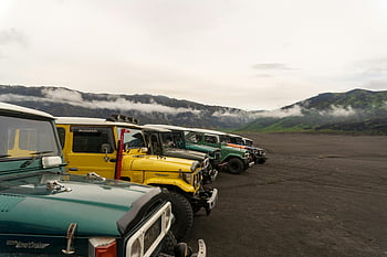 offroad vehicles, volcanic terrain, Mount Bromo, classic vehicles, mist-covered mountain, dirt road, adventure travel, outdoor exploration, jeep safari, travel photography, natural landscape