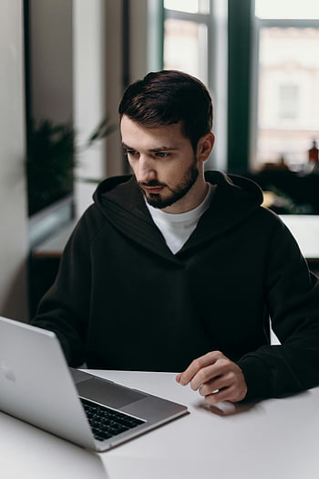 man in black hoodie, using Macbook, focused young man, laptop, desk, stylish home office, working, indoor, casual work, technology, productivity